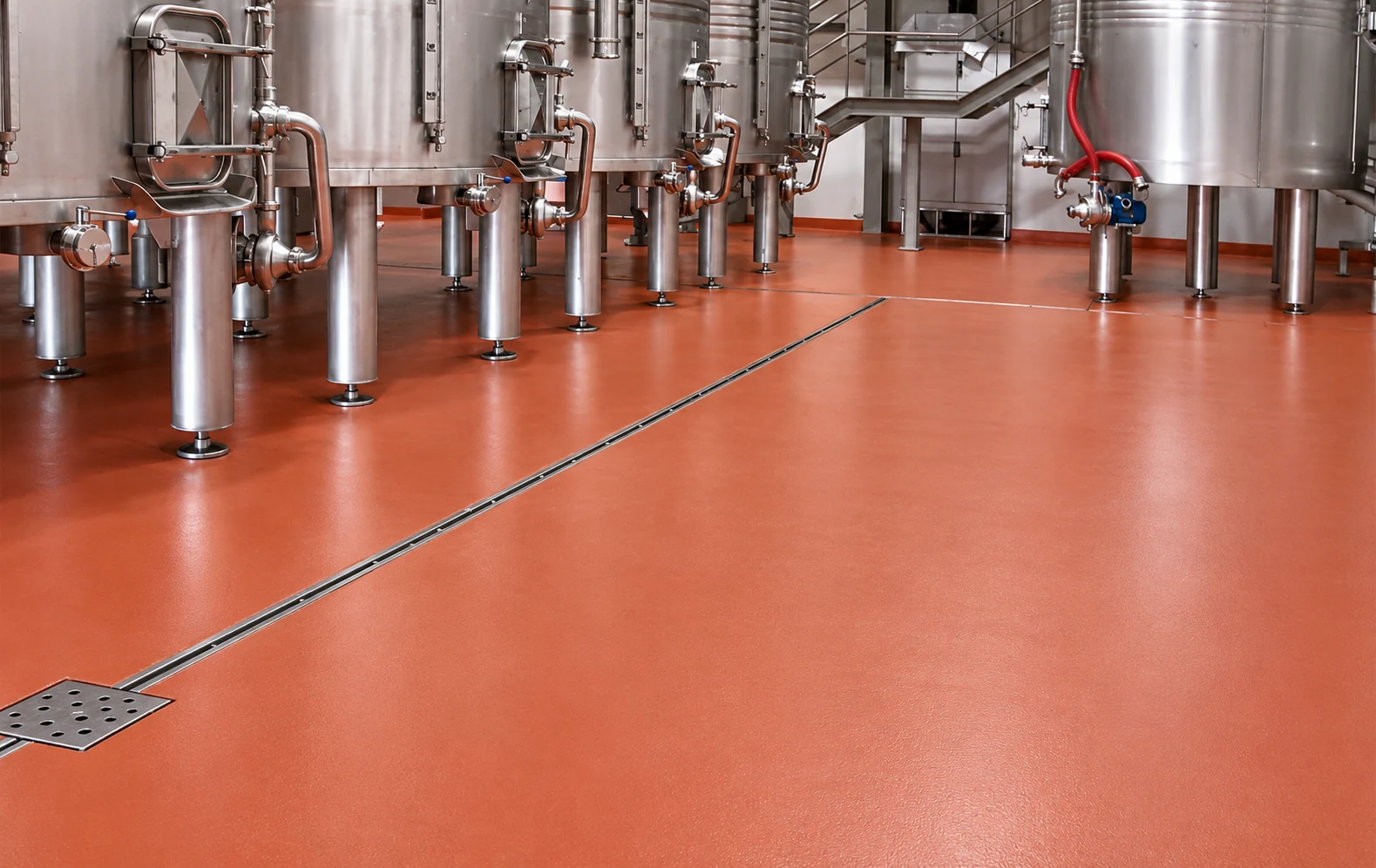 Red flooring around stainless-steel beverage processing tanks and a drainage channel
