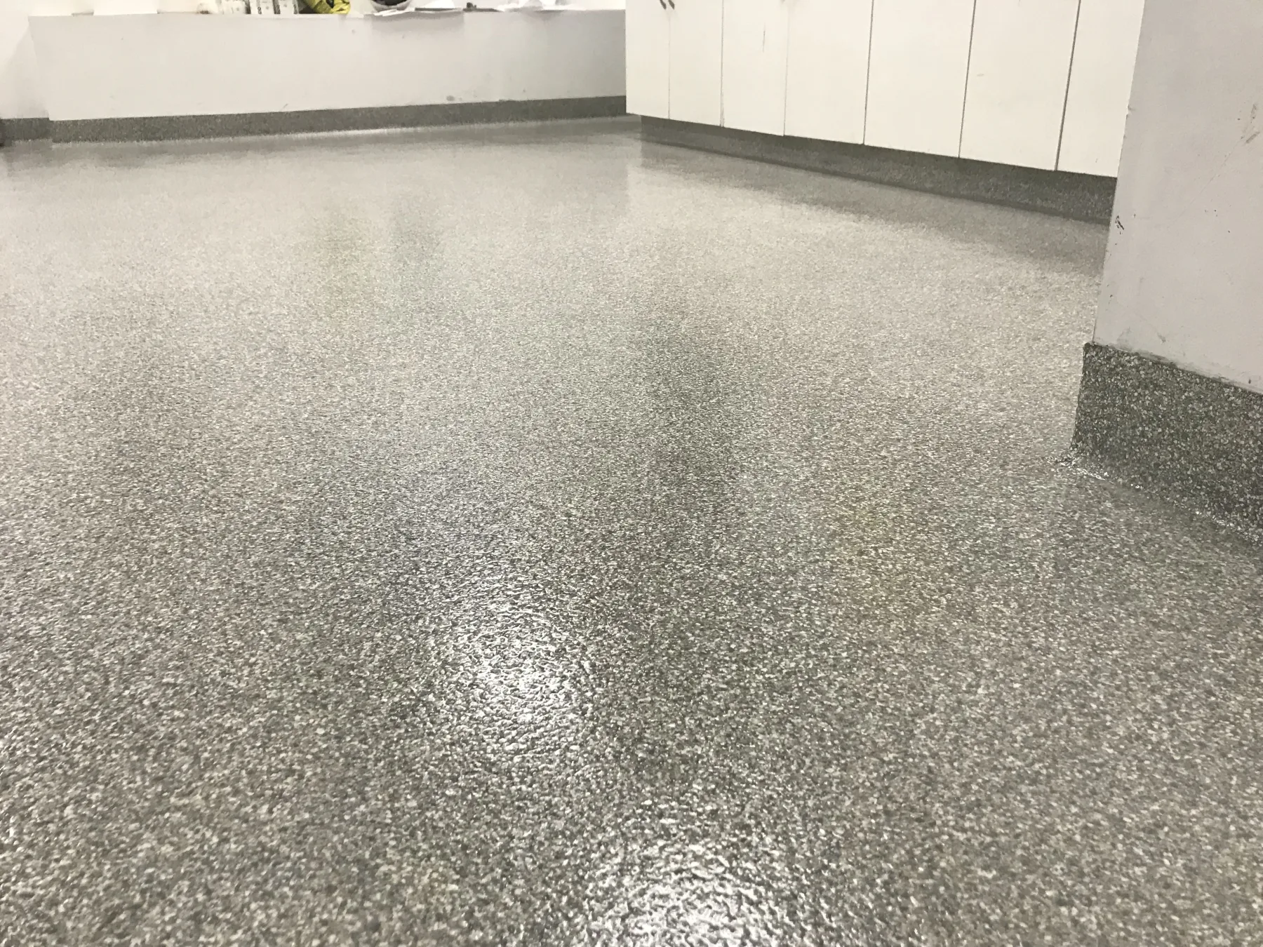 Grey decorative flake flooring with integral cove bases around cabinets and columns