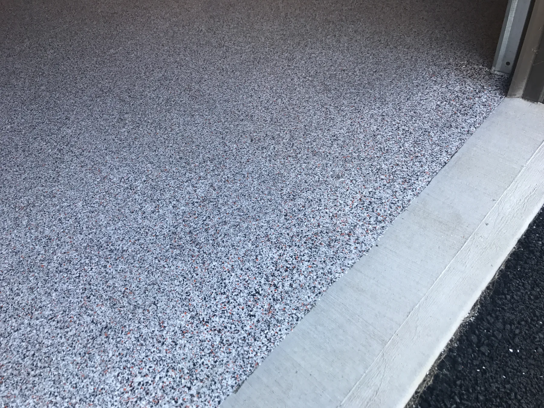 Close view of a grey, black and red decorative flake floor at a doorway threshold