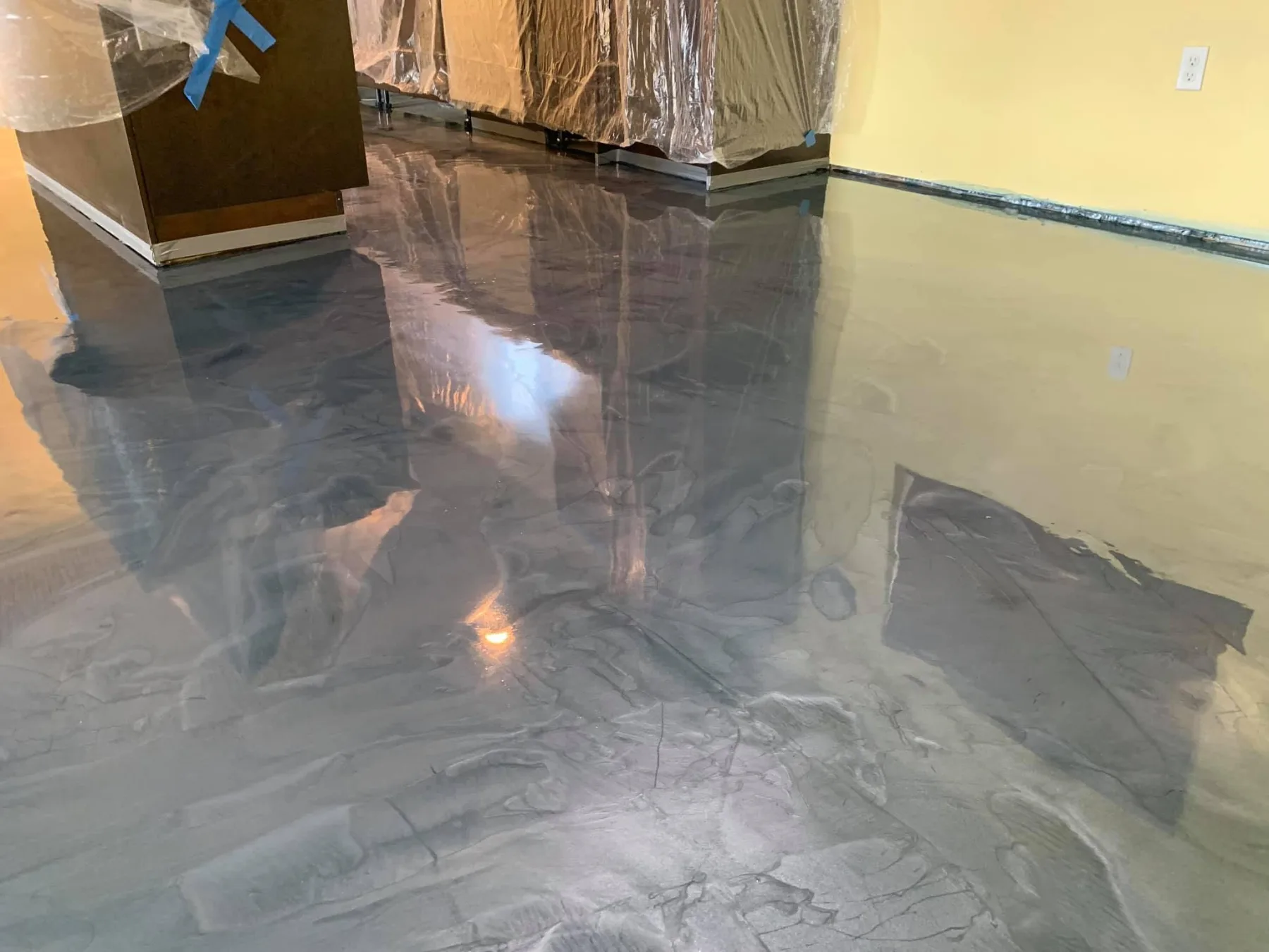 Glossy charcoal and silver metallic floor beneath protected cabinetry in a finished interior