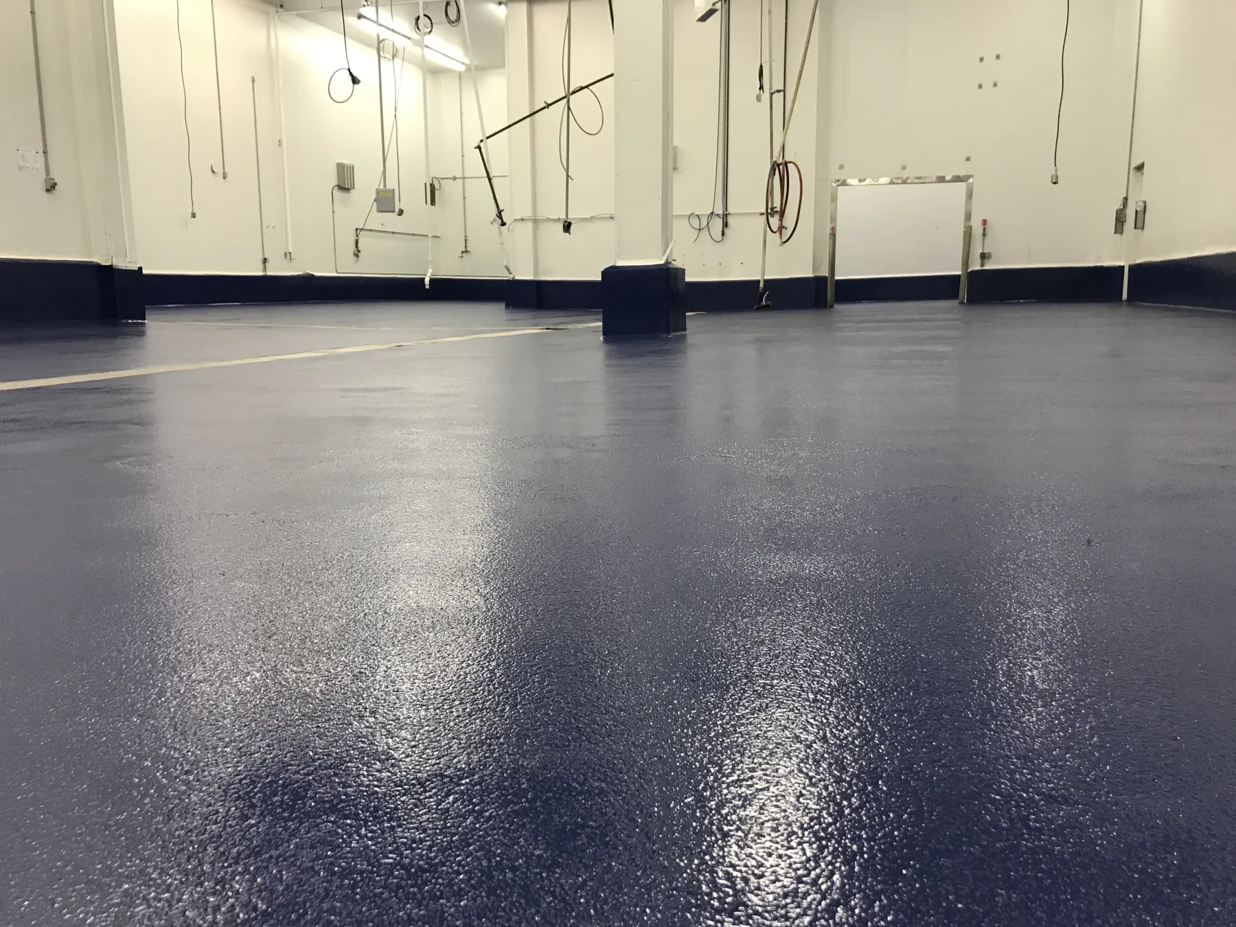 Low-angle view of textured dark-blue epoxy flooring across a large processing room