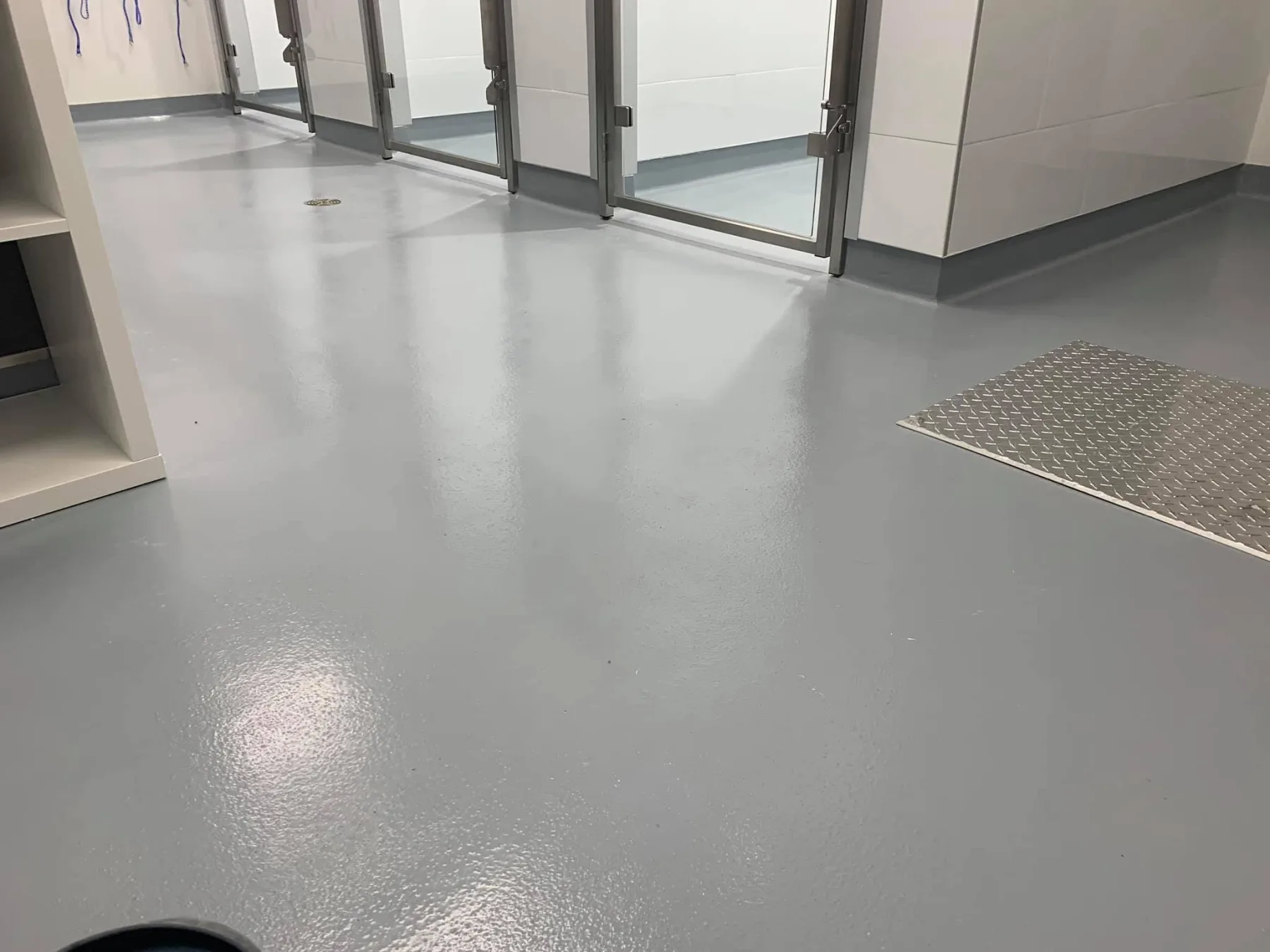 Light-grey seamless epoxy flooring with integral cove bases and stainless-steel access panels in a commercial washroom