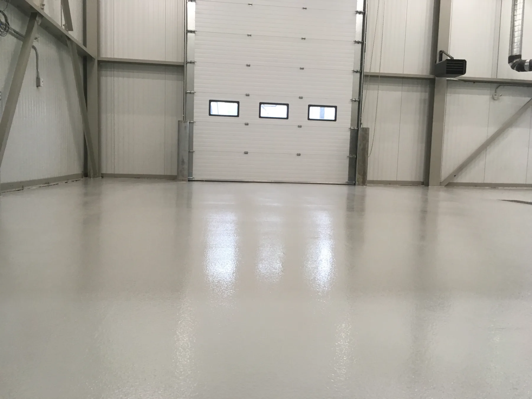 Glossy light-grey seamless epoxy floor in front of an industrial overhead door