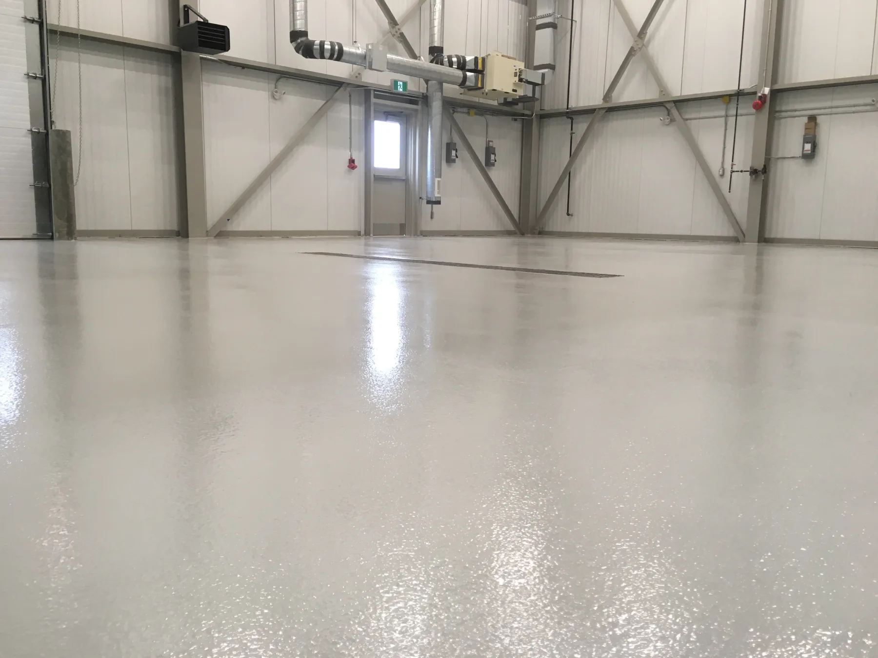Low-angle view of a glossy light-grey epoxy floor in an industrial facility