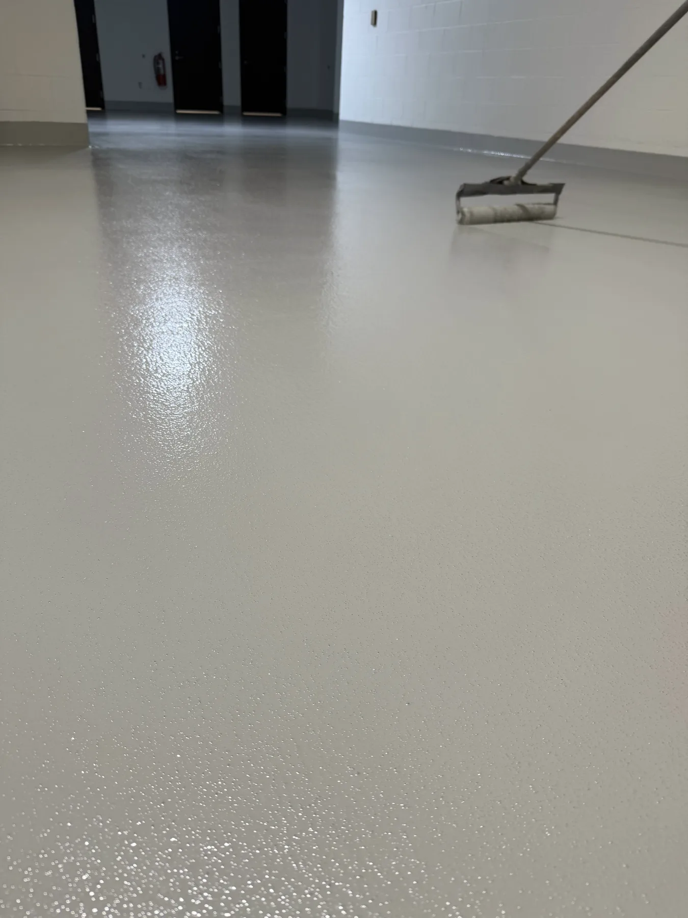 Fresh light-grey resin flooring being applied with a roller in a corridor