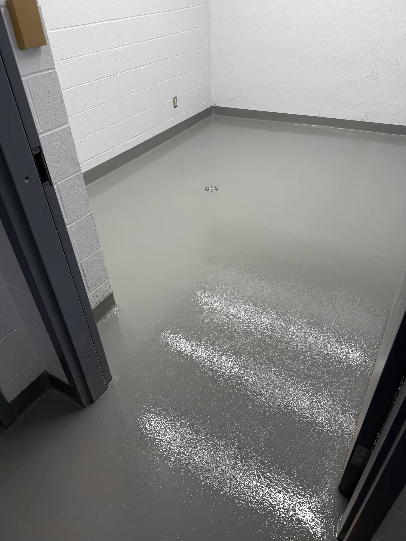 Textured grey seamless floor with integral cove base and a central drain in a small room