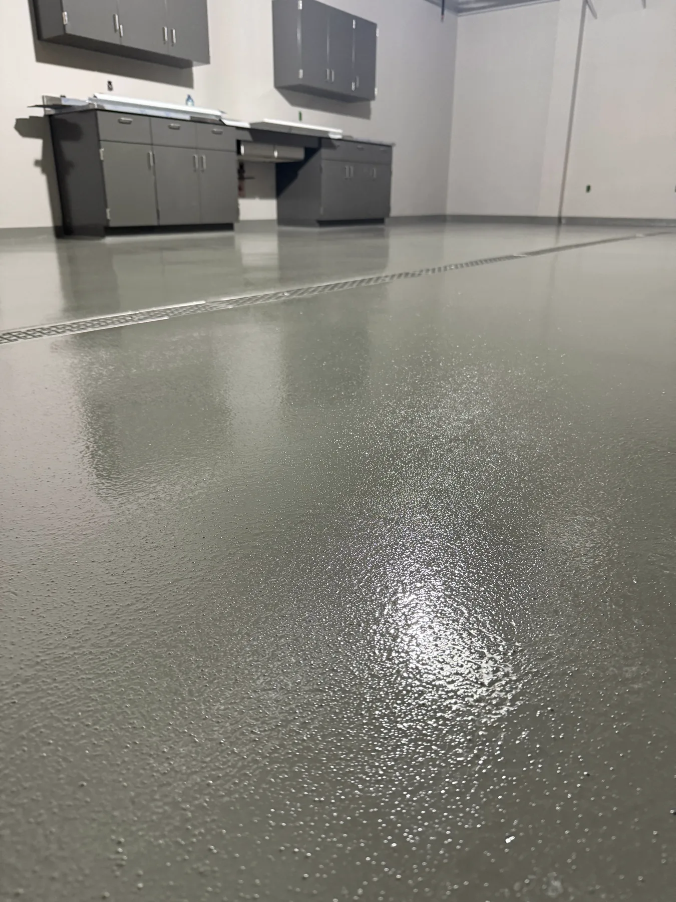 Low-angle view of a textured grey seamless floor with a linear drain in a utility room