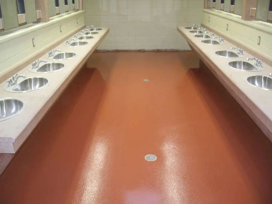Warm red seamless epoxy floor with drains beneath rows of washroom sinks