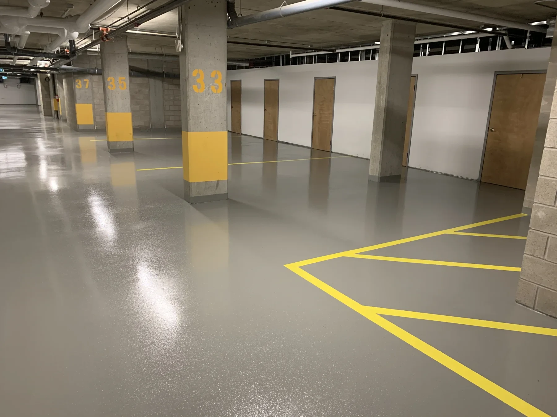 Glossy grey coating system with yellow parking lines and numbered concrete columns