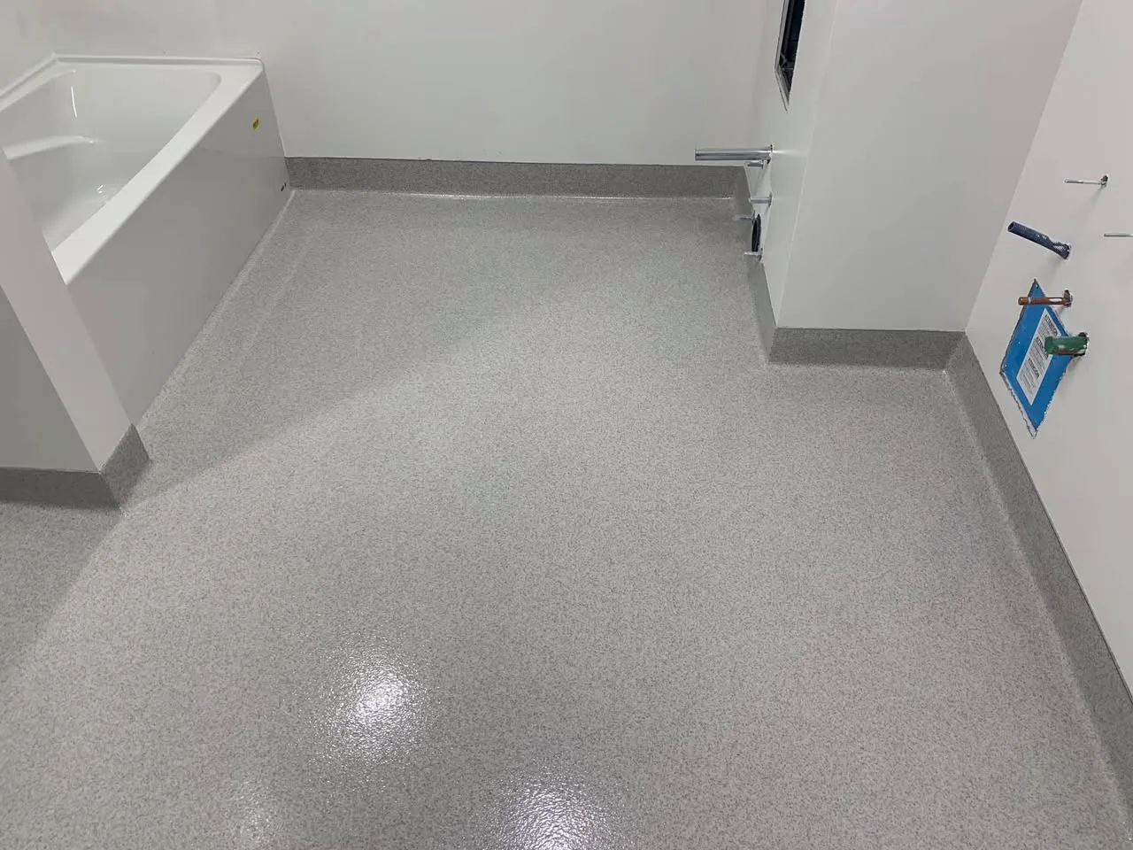 Light-grey quartz floor and cove bases installed around a bathtub area