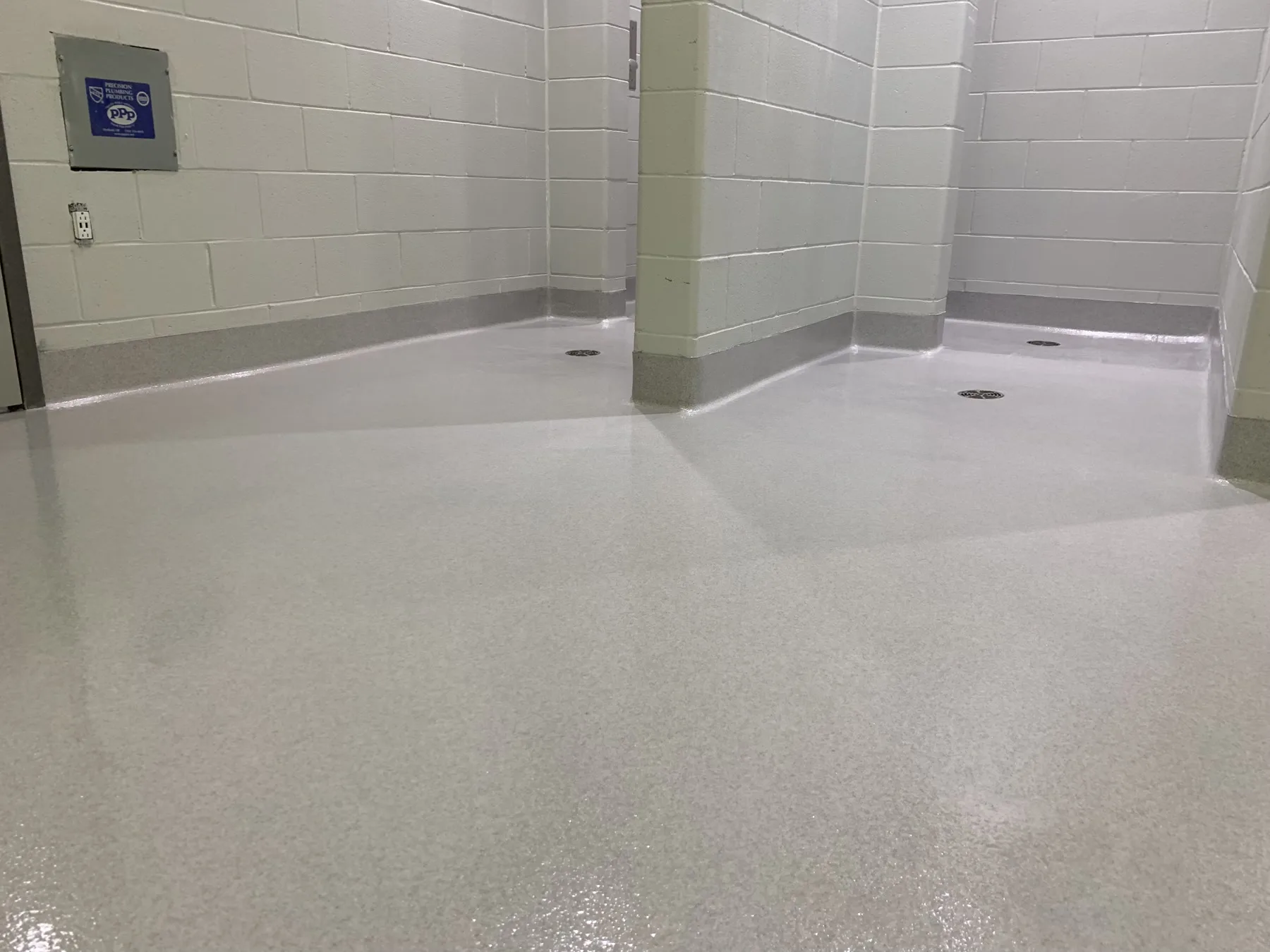 Light-grey quartz flooring with integral cove bases and multiple floor drains in a shower room