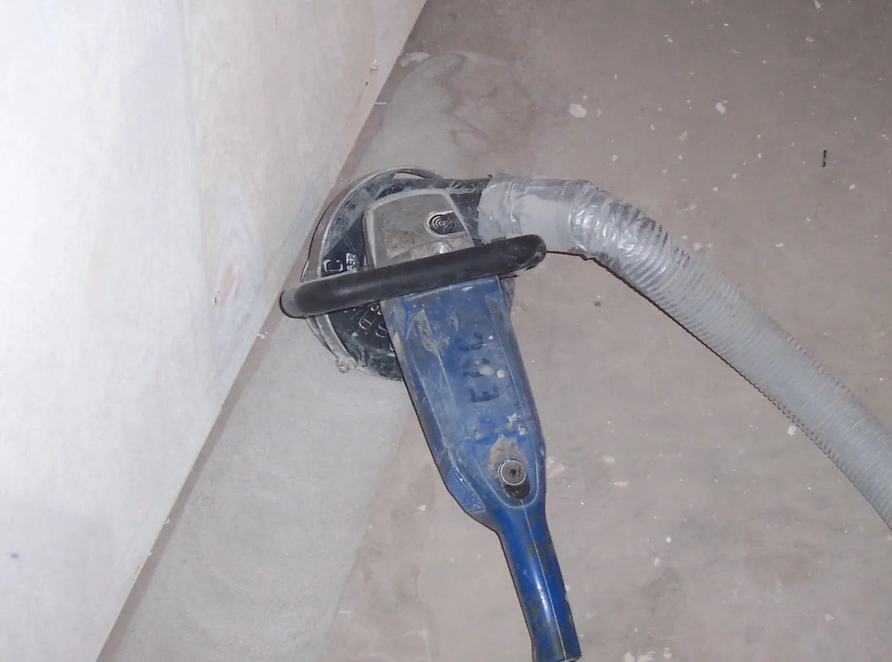 Hand-operated grinder connected to dust collection beside a concrete wall