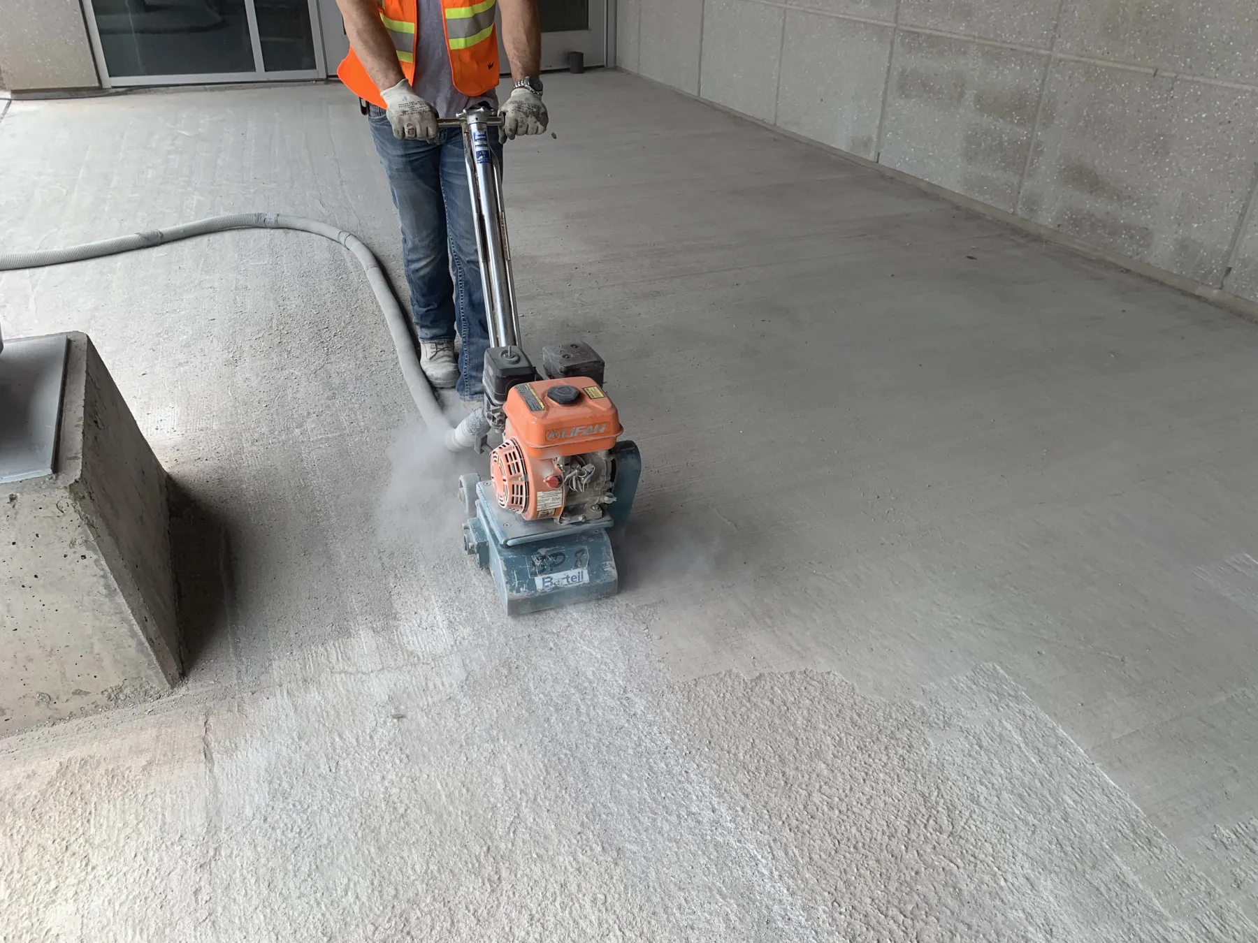 Worker using a compact surface-preparation machine on an exterior concrete entrance