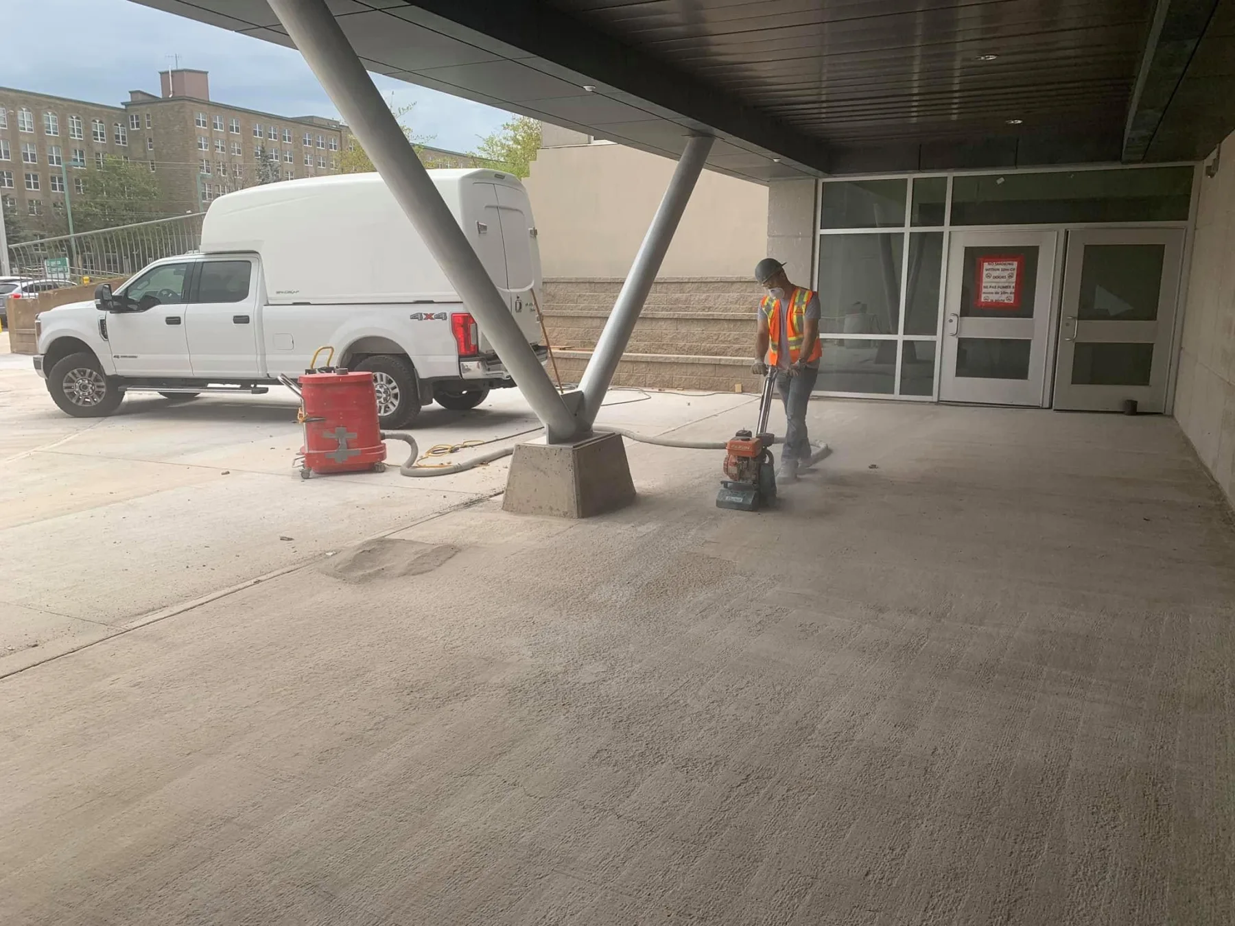 Worker using dust-controlled grinding equipment to prepare an exterior concrete entrance