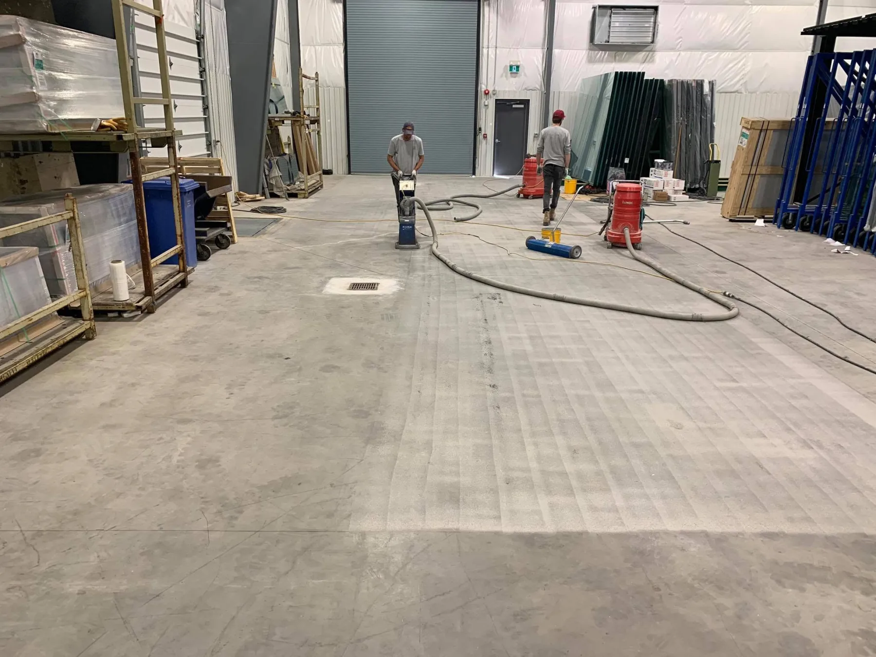Crew mechanically preparing a large concrete floor with grinding equipment and connected dust collection