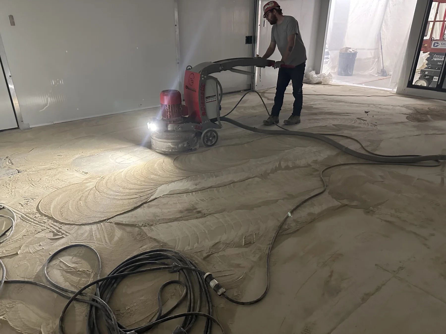 Worker mechanically grinding an interior concrete floor with connected dust control