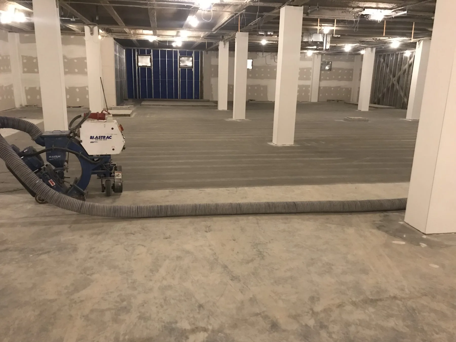 Shot-blasting equipment preparing a large concrete floor around structural columns