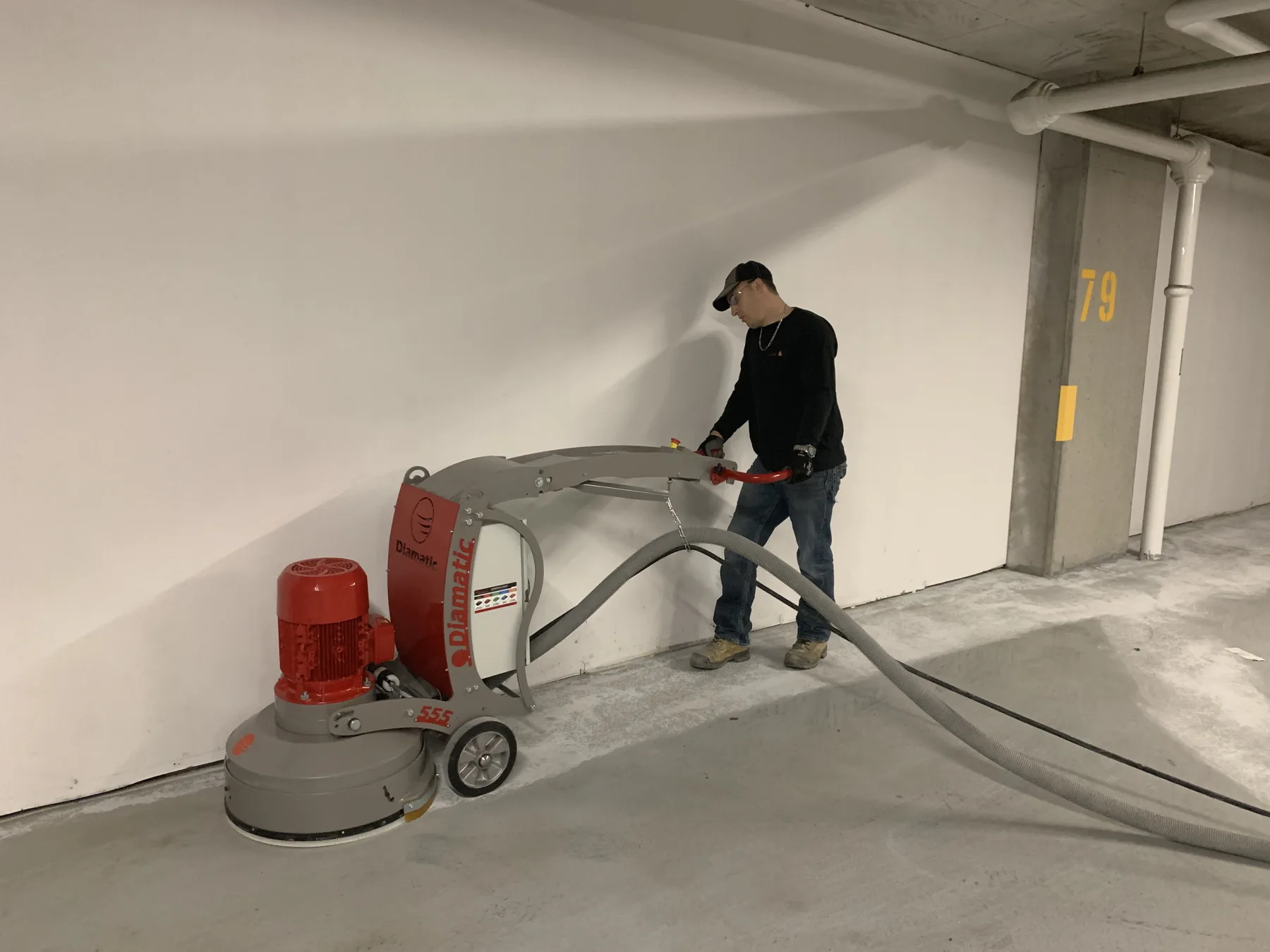 Worker operating a dust-controlled planetary grinder along a parking-garage perimeter