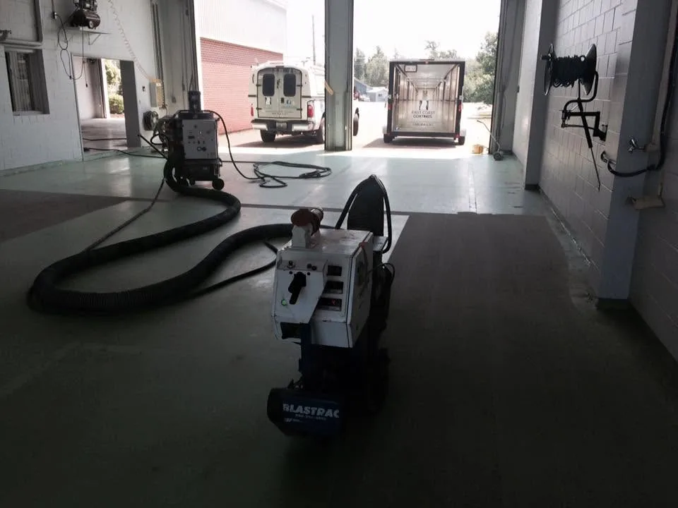 Shot-blasting equipment with dust-control hoses preparing a concrete service-bay floor
