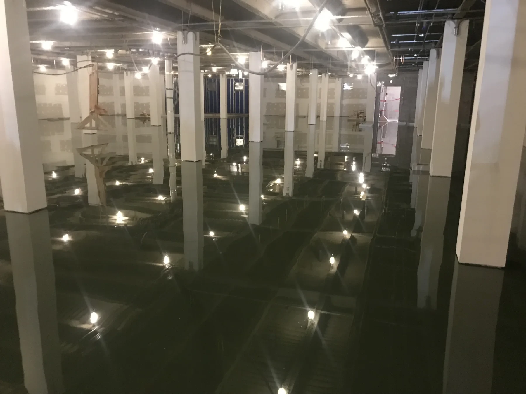 Glossy dark waterproofing membrane installed across a large columned interior