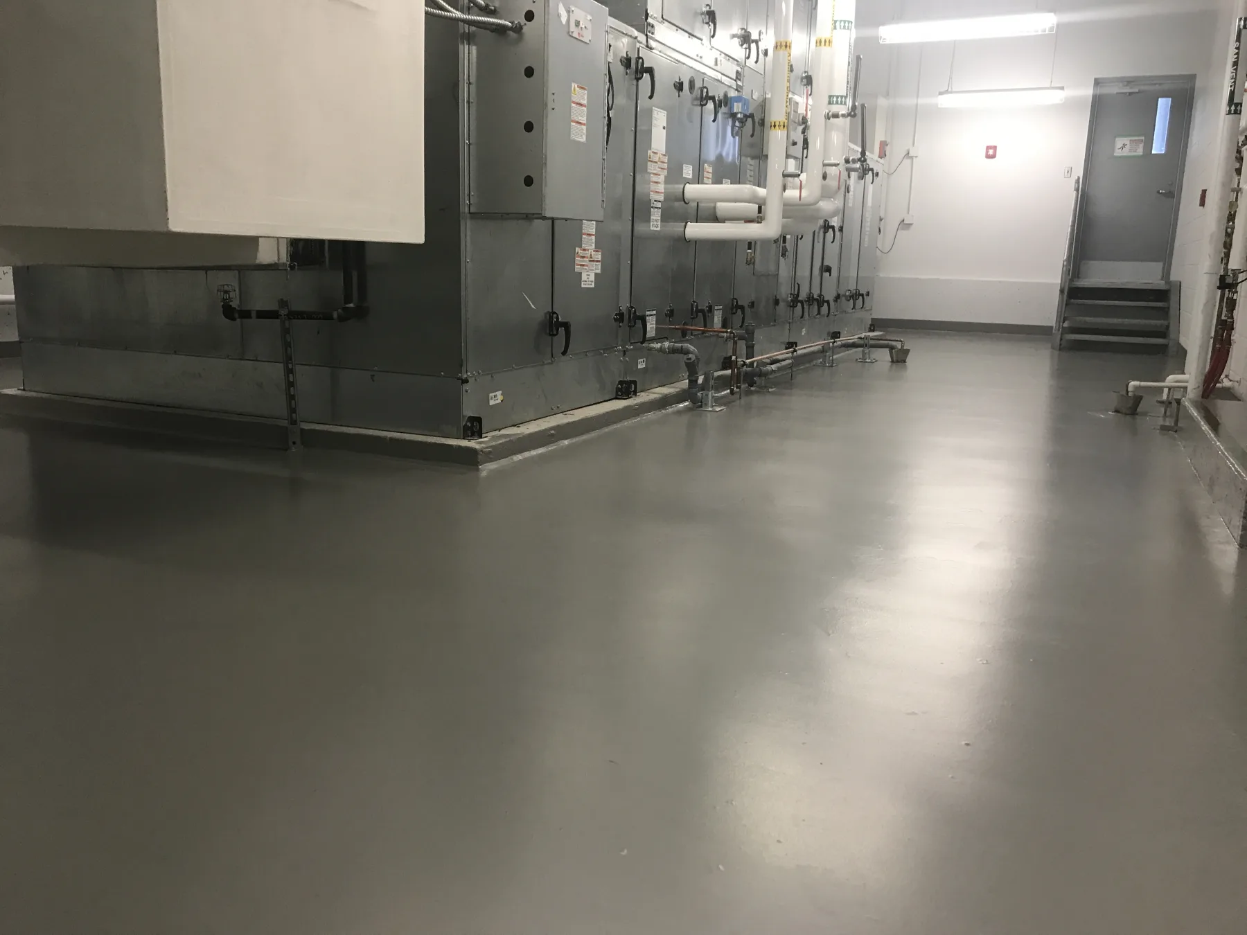 Continuous grey waterproof membrane flooring installed around large mechanical equipment and pipework