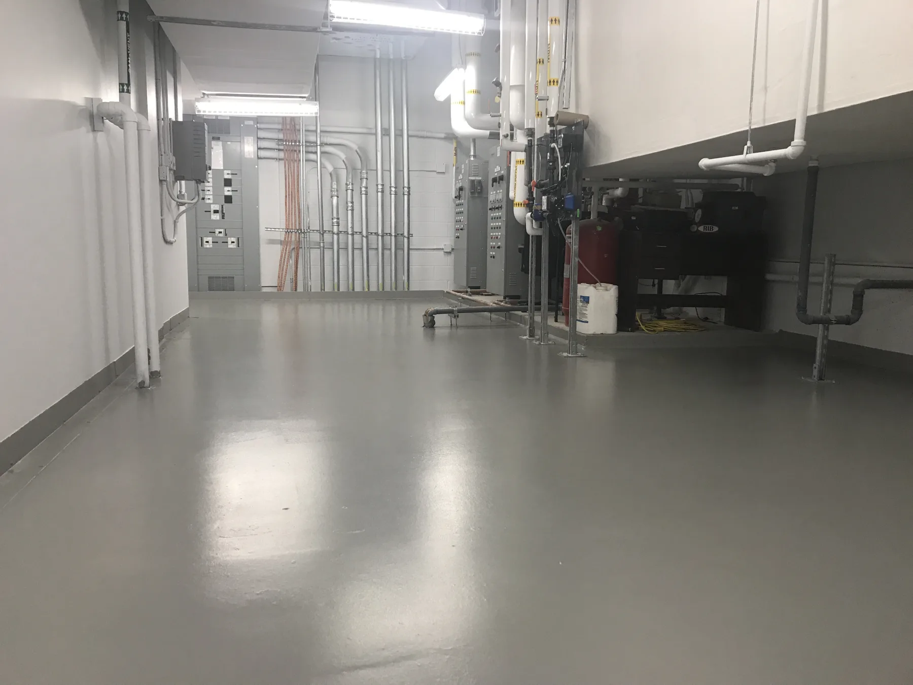 Grey waterproof membrane flooring with sealed perimeter details in a mechanical room